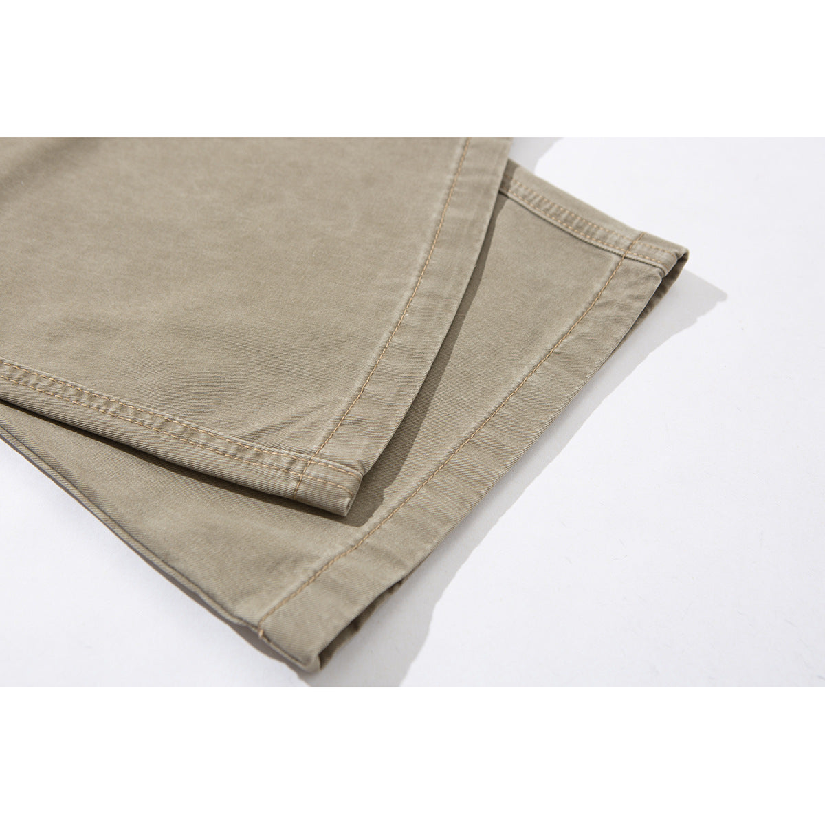Close-up of the stitched hems and wide legs of taupe pants, folded over one another.