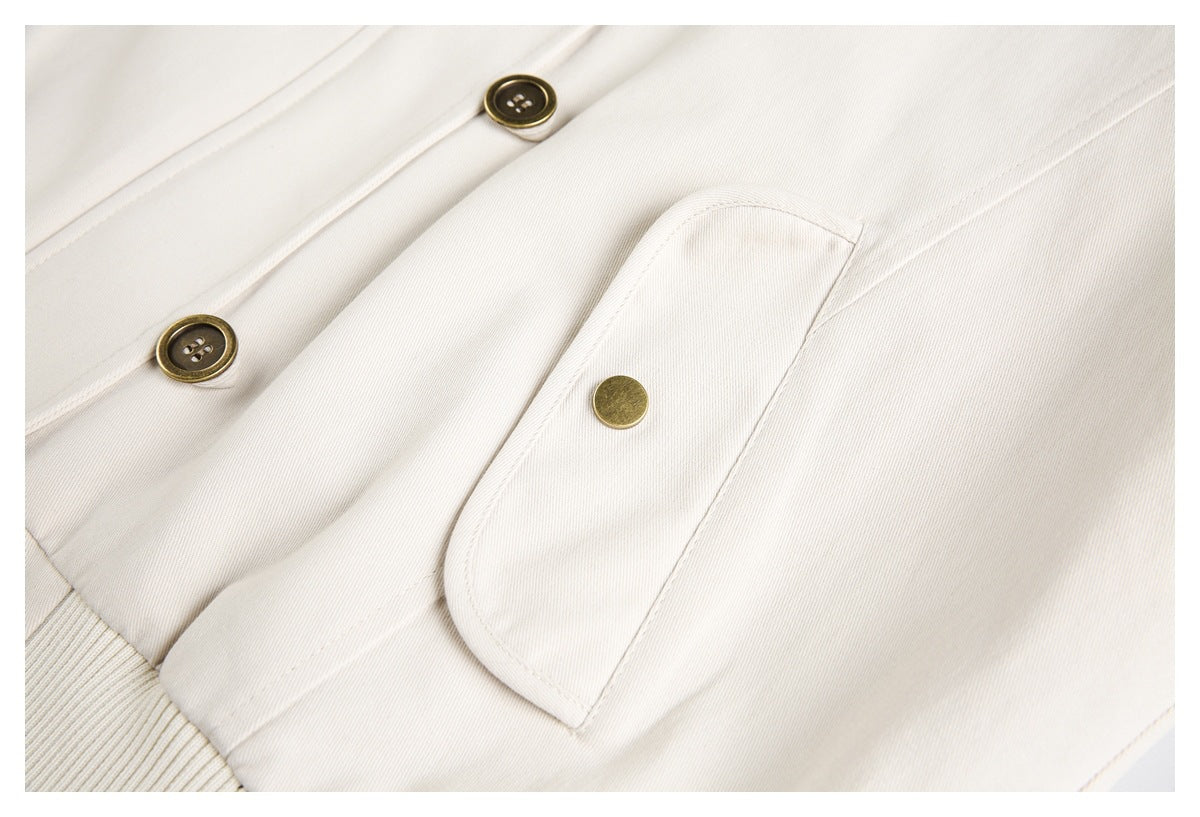 Close-up of an ivory jacket pocket flap with brass-colored buttons and visible stitching.