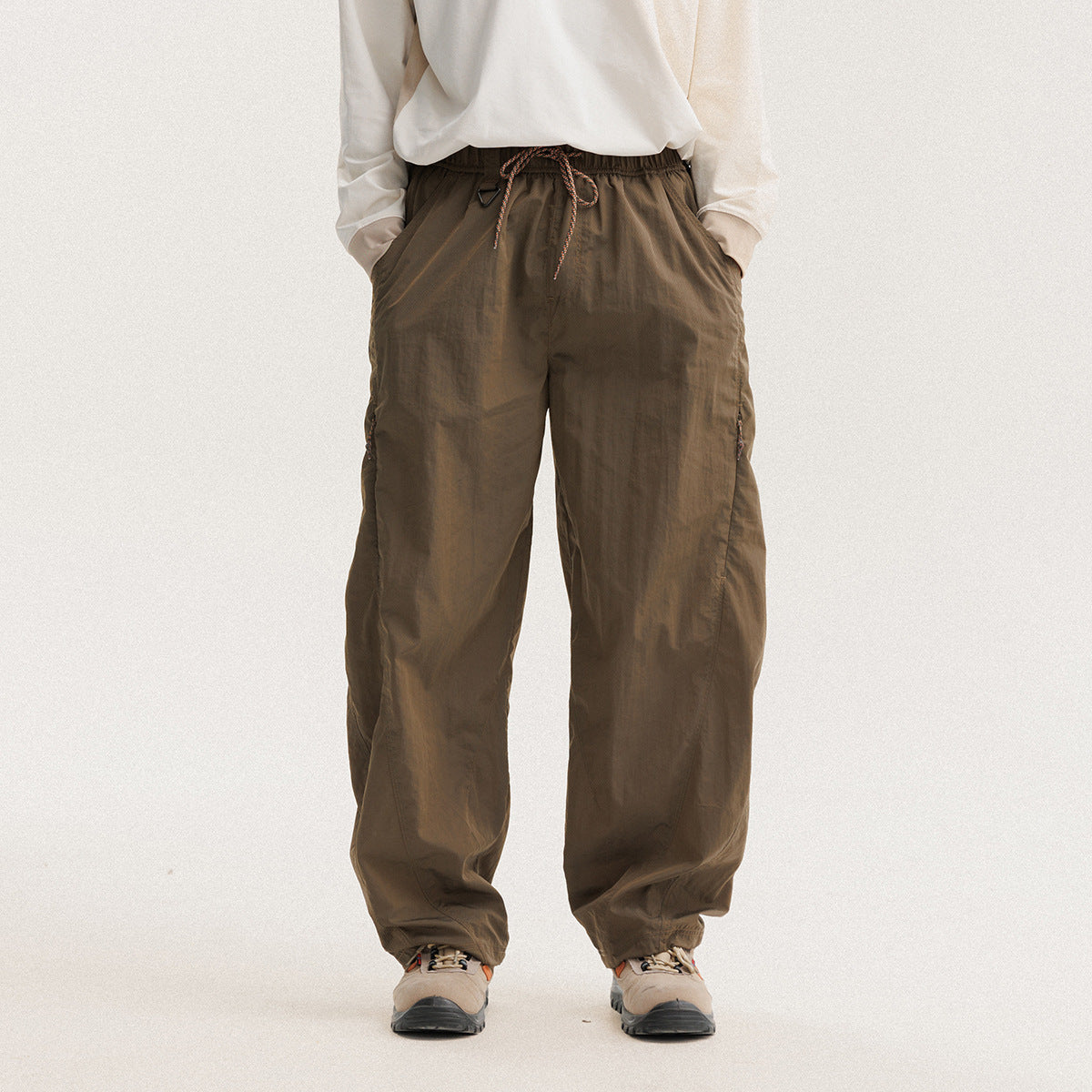 Front view of a model wearing loose dark-brown pants with a drawstring waist and side pockets.