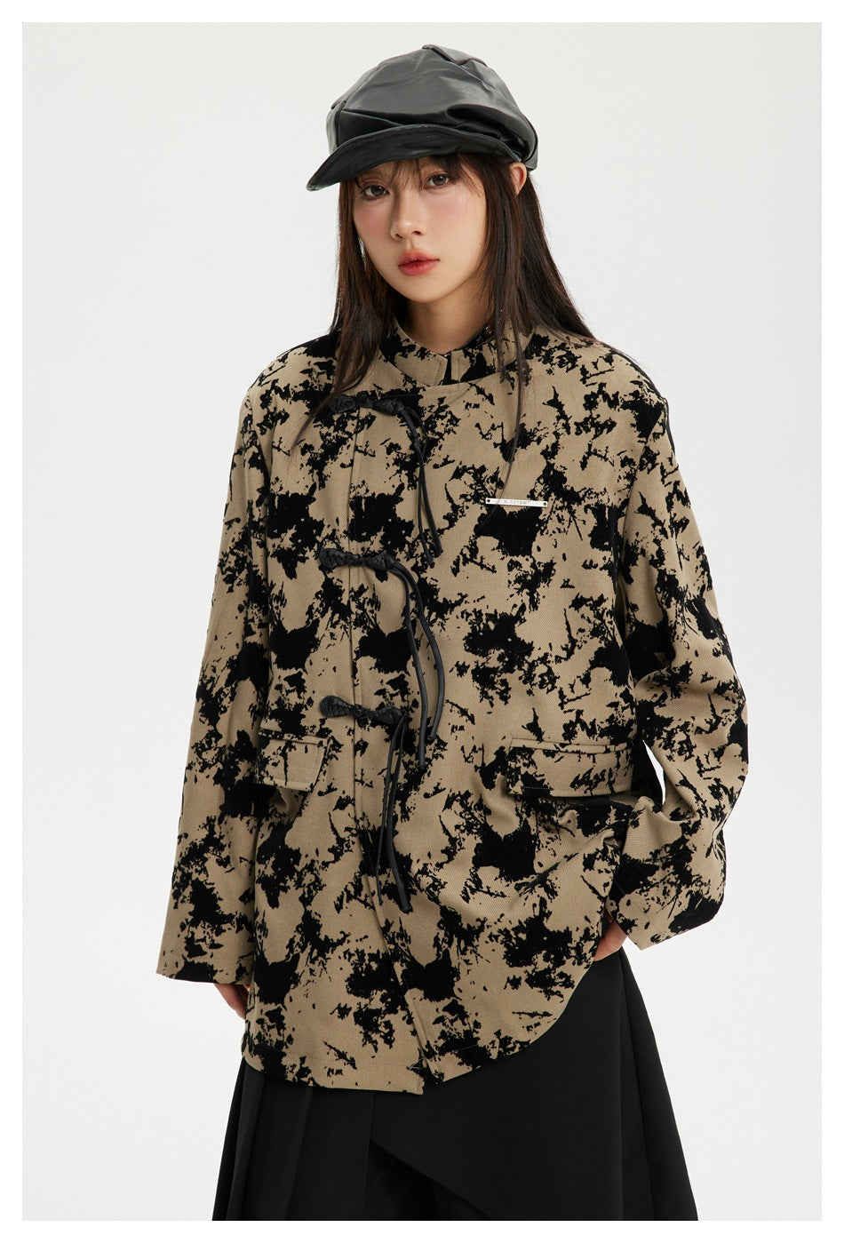 Model wearing an oversized taupe jacket with black abstract print, frog closures, and flap pockets.