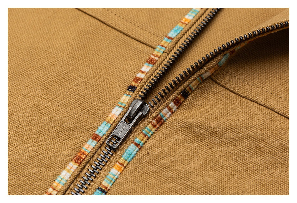 Close-up of a metal zipper and multicolor patterned trim on tan jacket fabric.