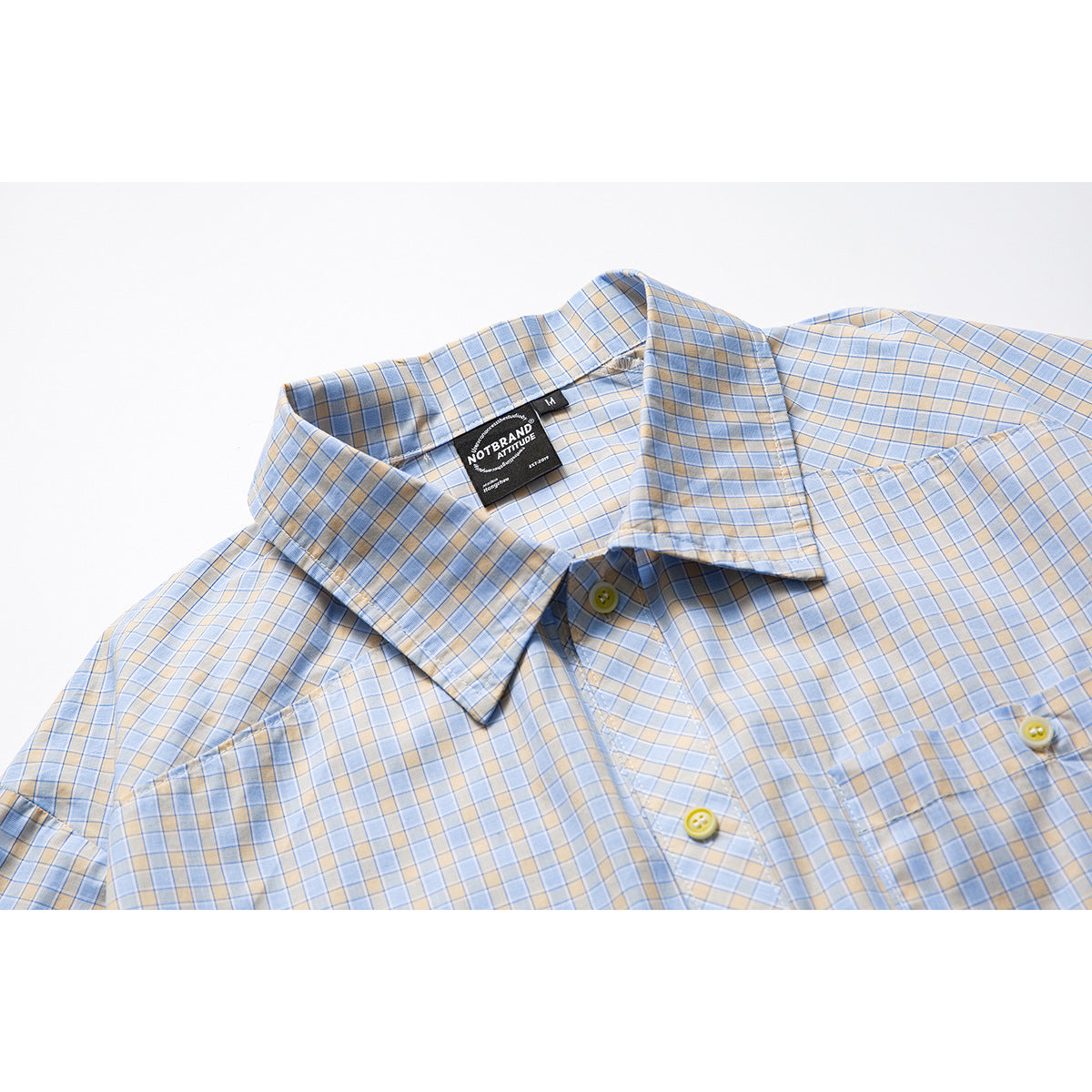 Close-up of a light blue and beige plaid shirt collar, yellow buttons, and sewn-in neck label.