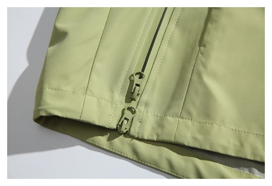 Close-up of two olive zipper sliders at the lower edge of the pale olive jacket.
