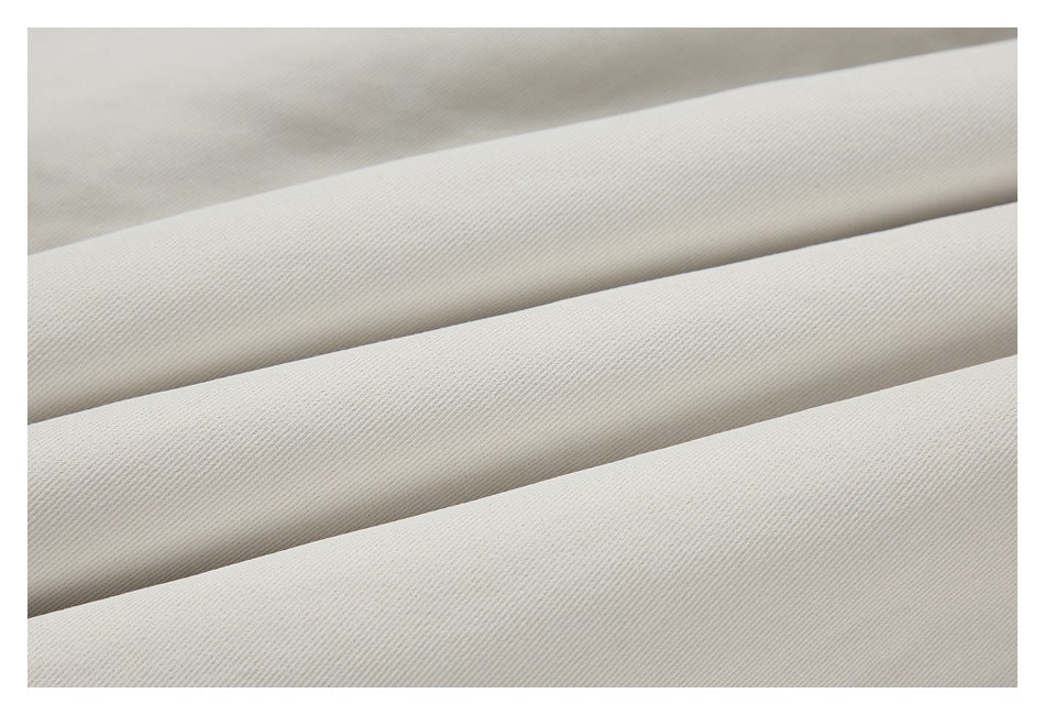 Close-up of pale beige garment fabric arranged in broad folds, showing its fine diagonal texture.