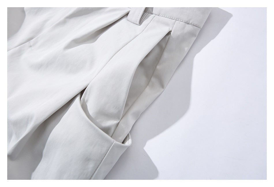 Close-up of a pocket opening and belt loop on pale gray trousers.