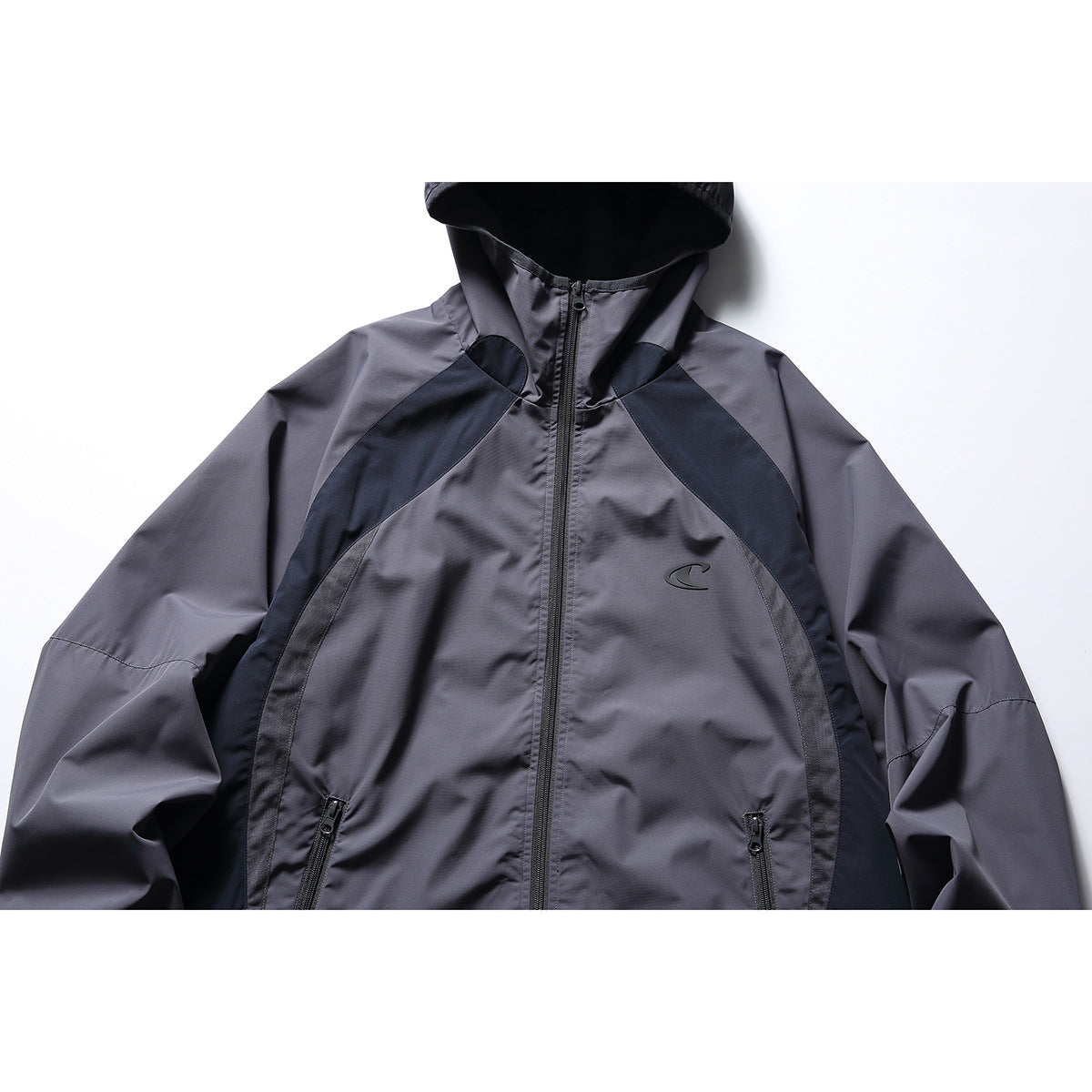 Close-up front of a charcoal-gray hooded jacket with black panels, a center zipper, and zip pockets.