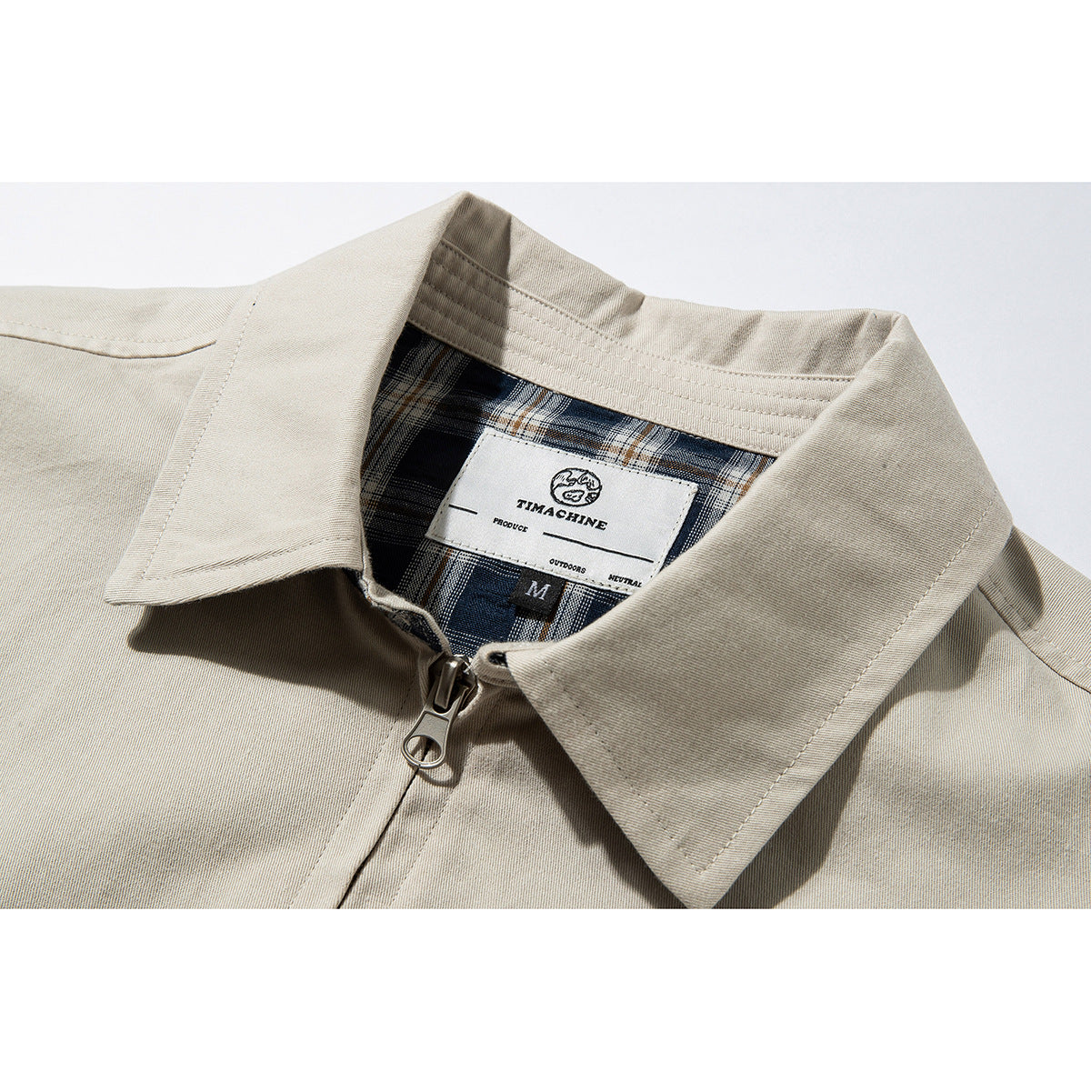 Close-up of a beige jacket collar, zipper, and blue plaid inner lining with a sewn neck label.