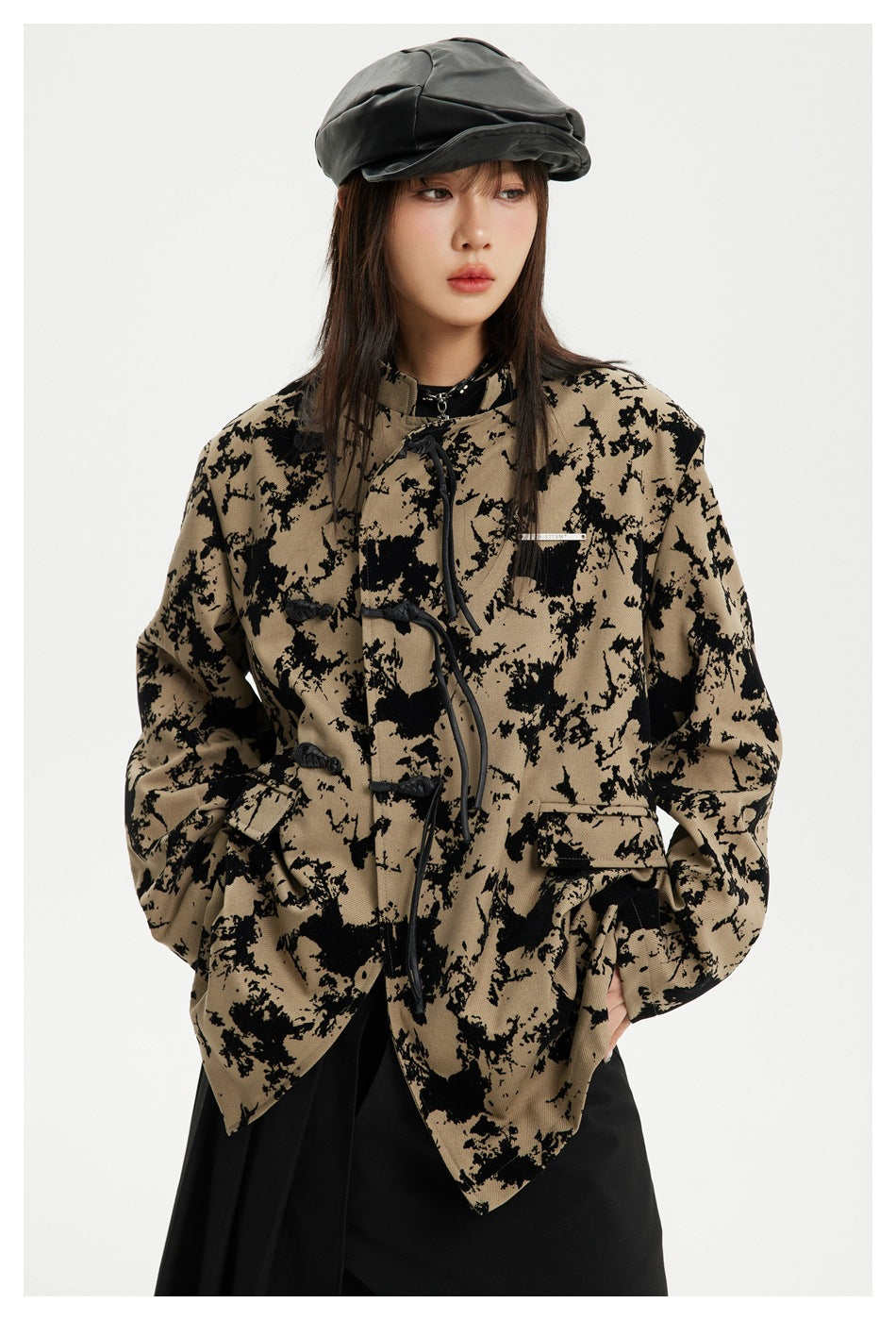 Front view of a model in an oversized tan-and-black patterned jacket with toggle closures and flap pockets.