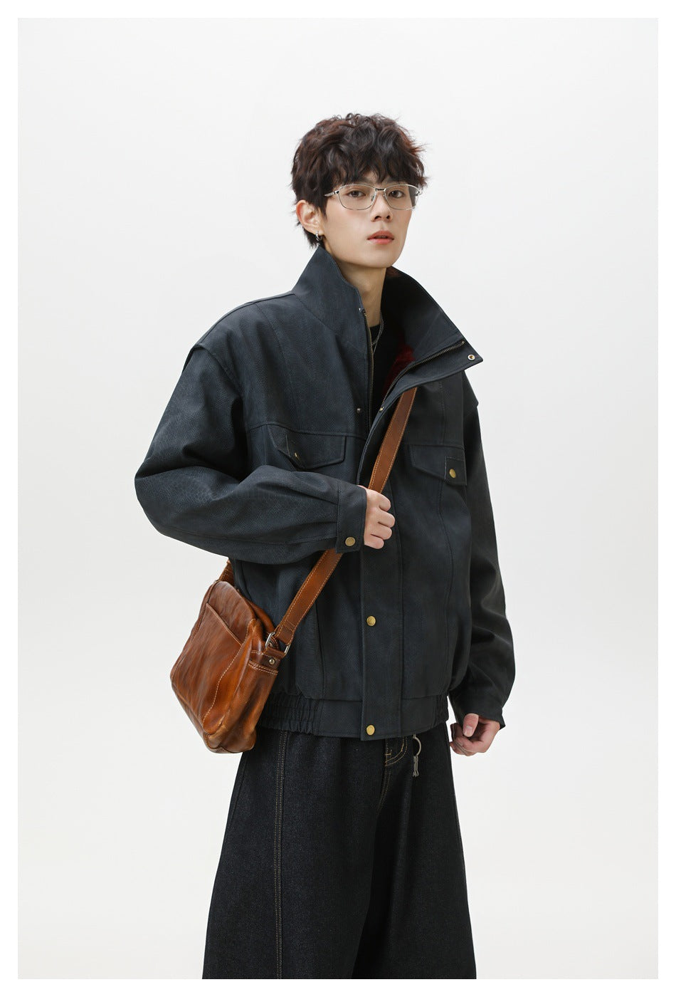 Model wearing a dark charcoal high-collar jacket with brass-tone buttons and flap pockets, paired with dark jeans.