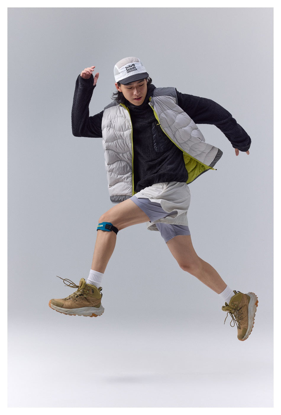 Hiker in motion wearing an open white quilted vest with lime lining over a dark fleece top and light shorts.