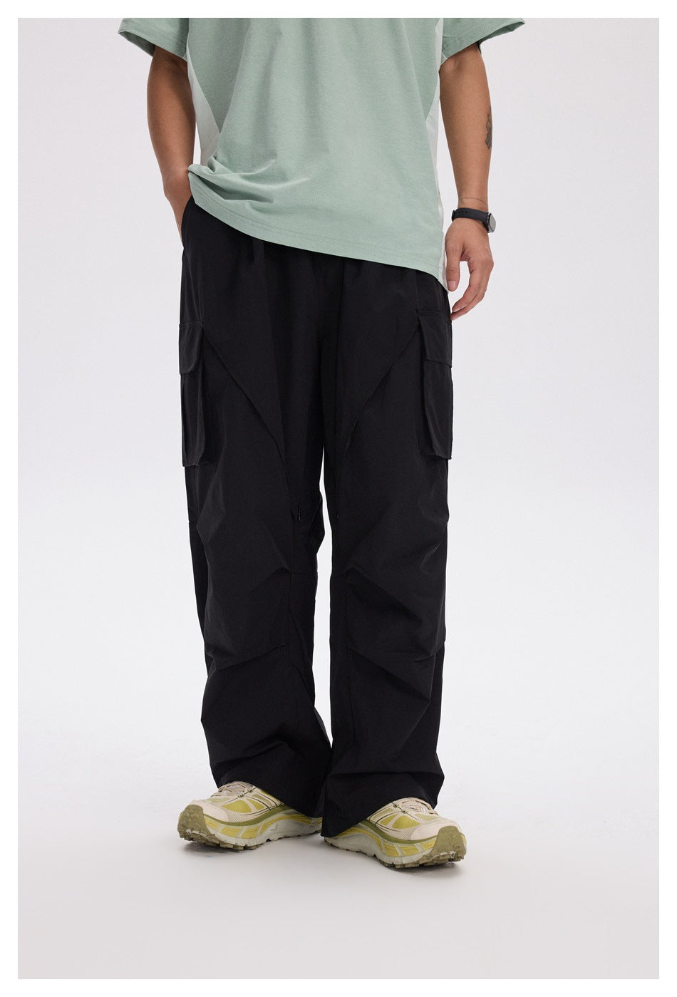 Front view of a model wearing loose black cargo pants with flap cargo pockets and a pale green shirt.