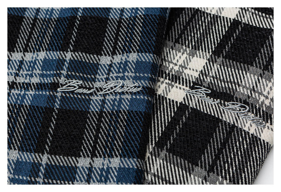 Close-up of embroidered script on blue plaid and black-and-white plaid shirt fabric.