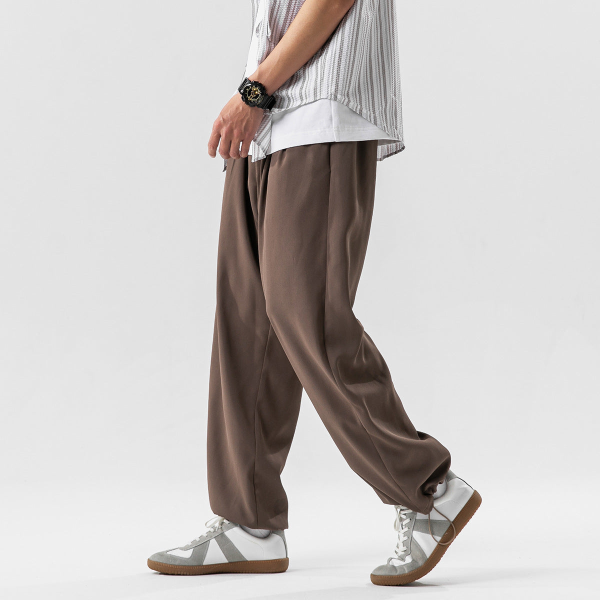 A person wears loose brown trousers with wide straight legs and sneakers, shown from waist to feet.