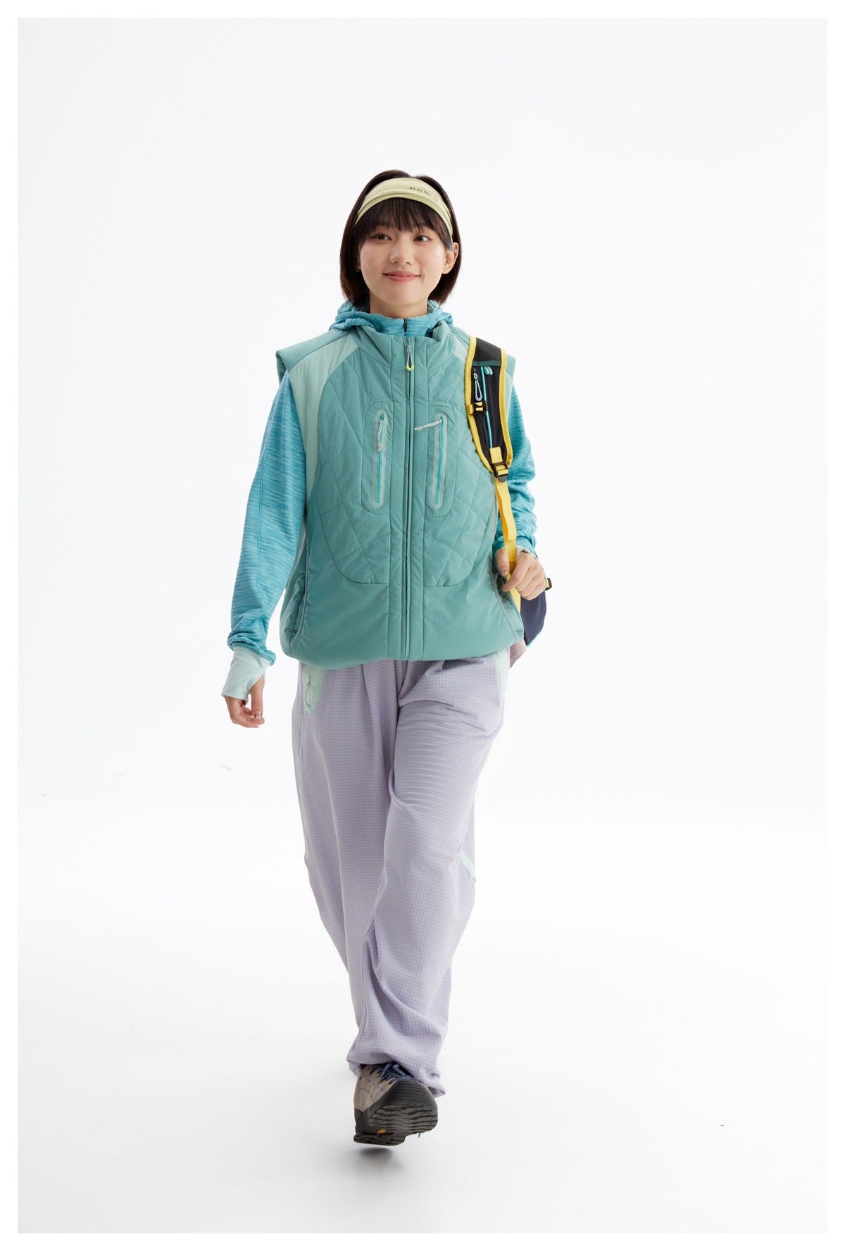 Model wearing a teal quilted zip vest with chest pockets over a turquoise top, paired with lavender pants.