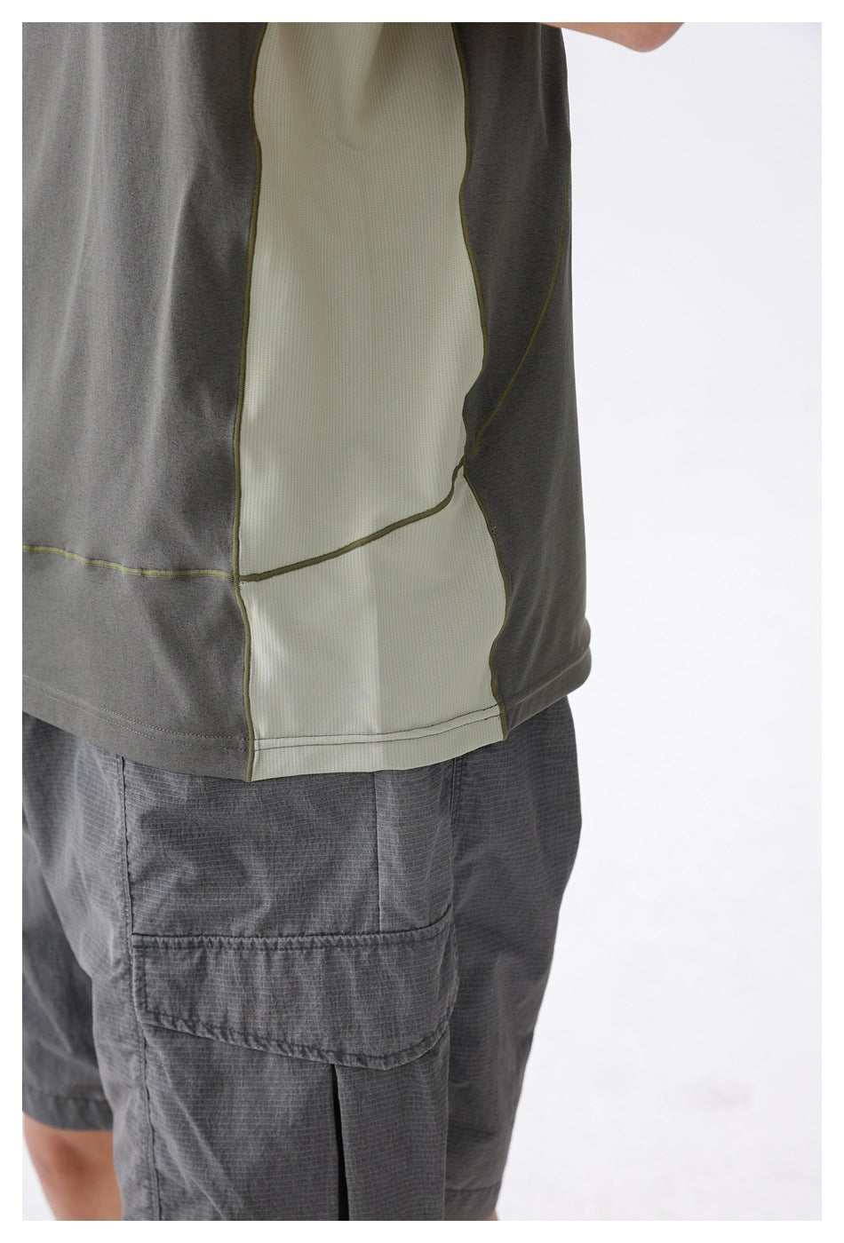 Close-up of the tank's pale mesh side panel and contrast stitching above a gray cargo-short pocket.