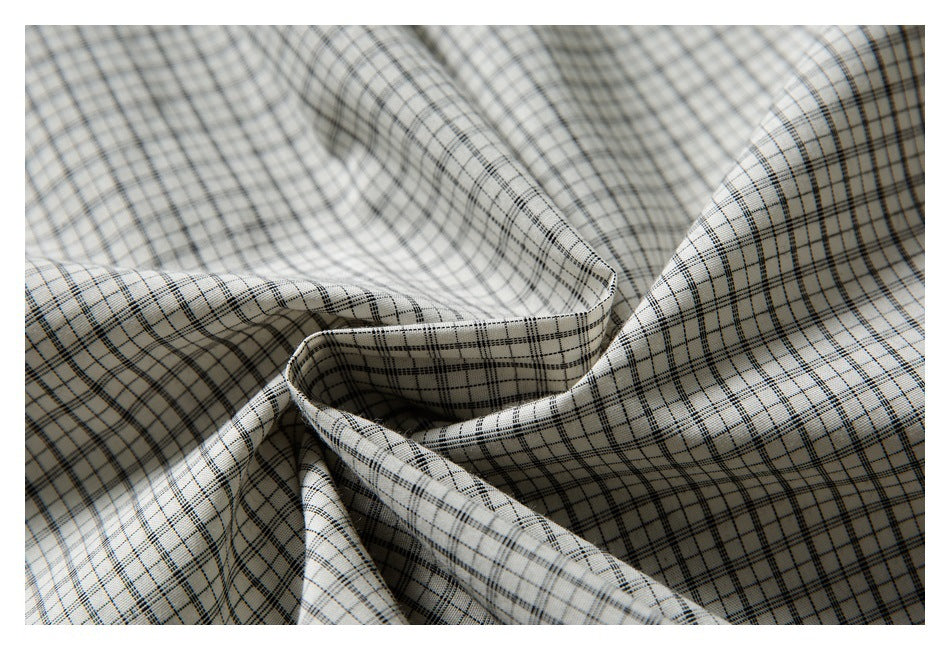 Close-up of off-white fabric with a fine black and gray plaid pattern arranged in soft folds.