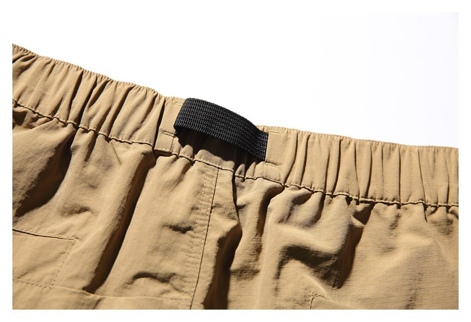 Close-up of the tan shorts' gathered waistband and black webbing loop.