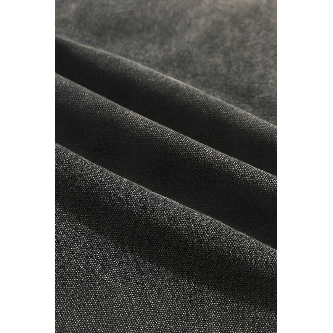 Macro view of the charcoal jacket’s textured fabric folded into soft ridges.