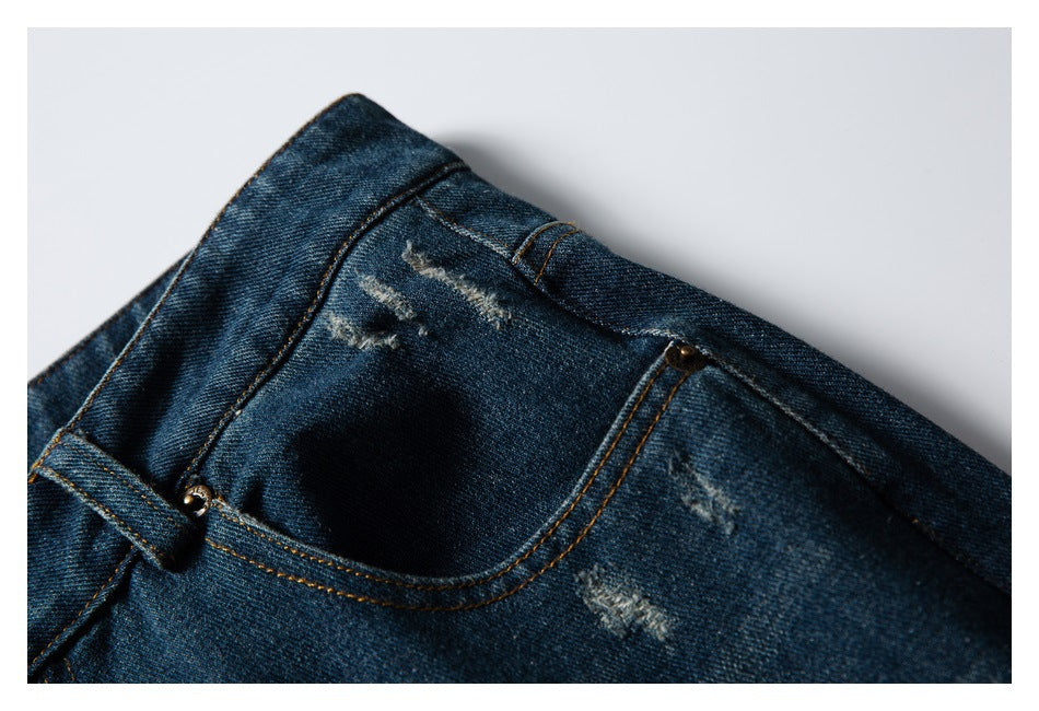 Close-up of a pocket and distressed marks on dark blue jeans with orange stitching.