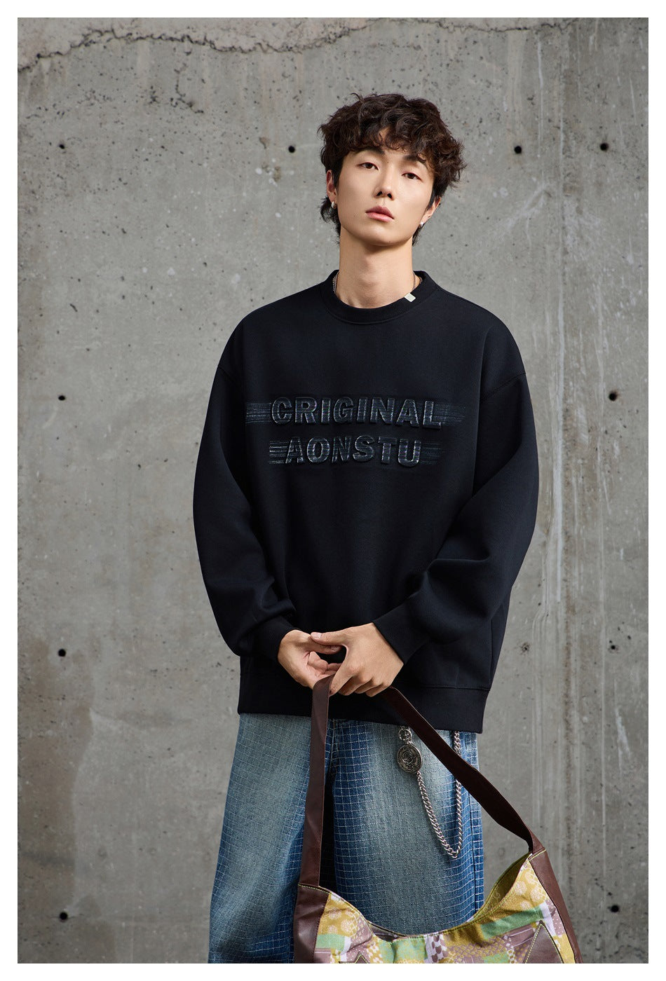 Front view of a model wearing a black crewneck sweatshirt with raised lettering and light blue patterned jeans.