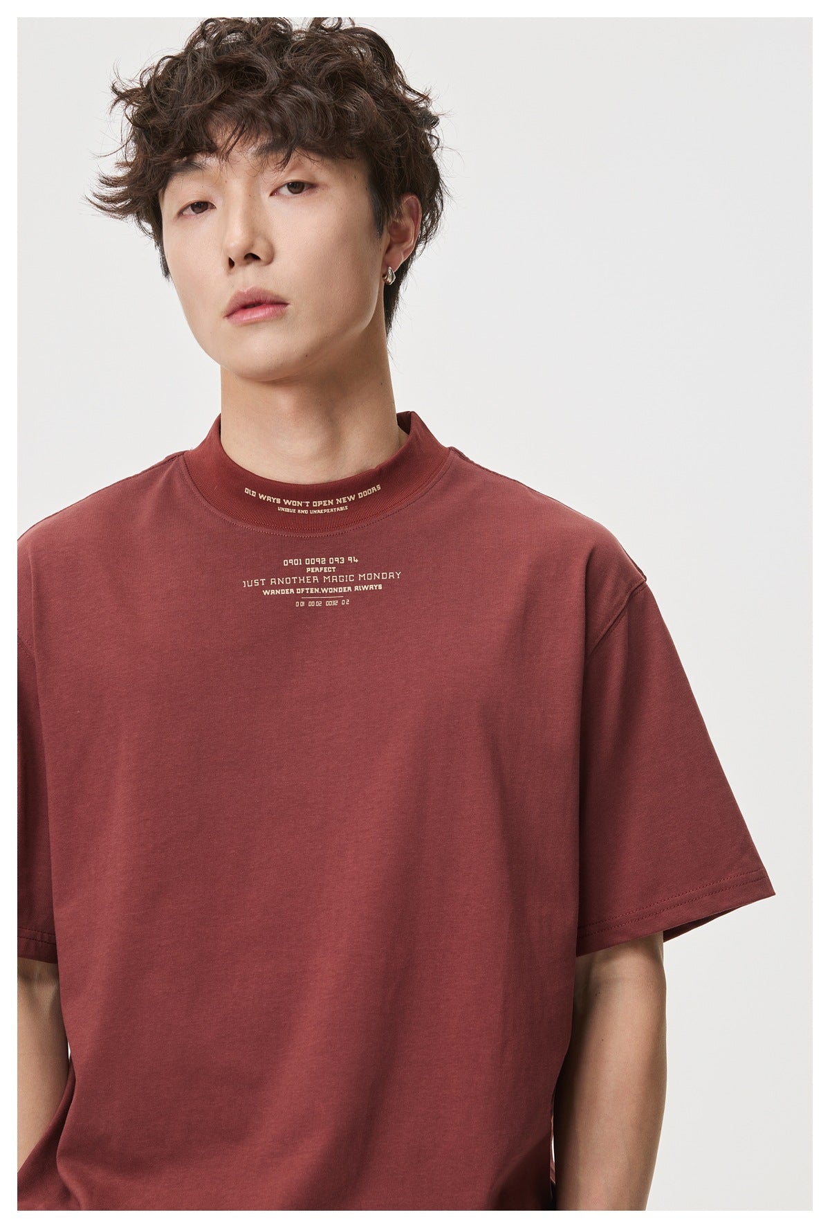Close view of a burgundy T-shirt on a model, showing small cream text at the high neckline and chest.