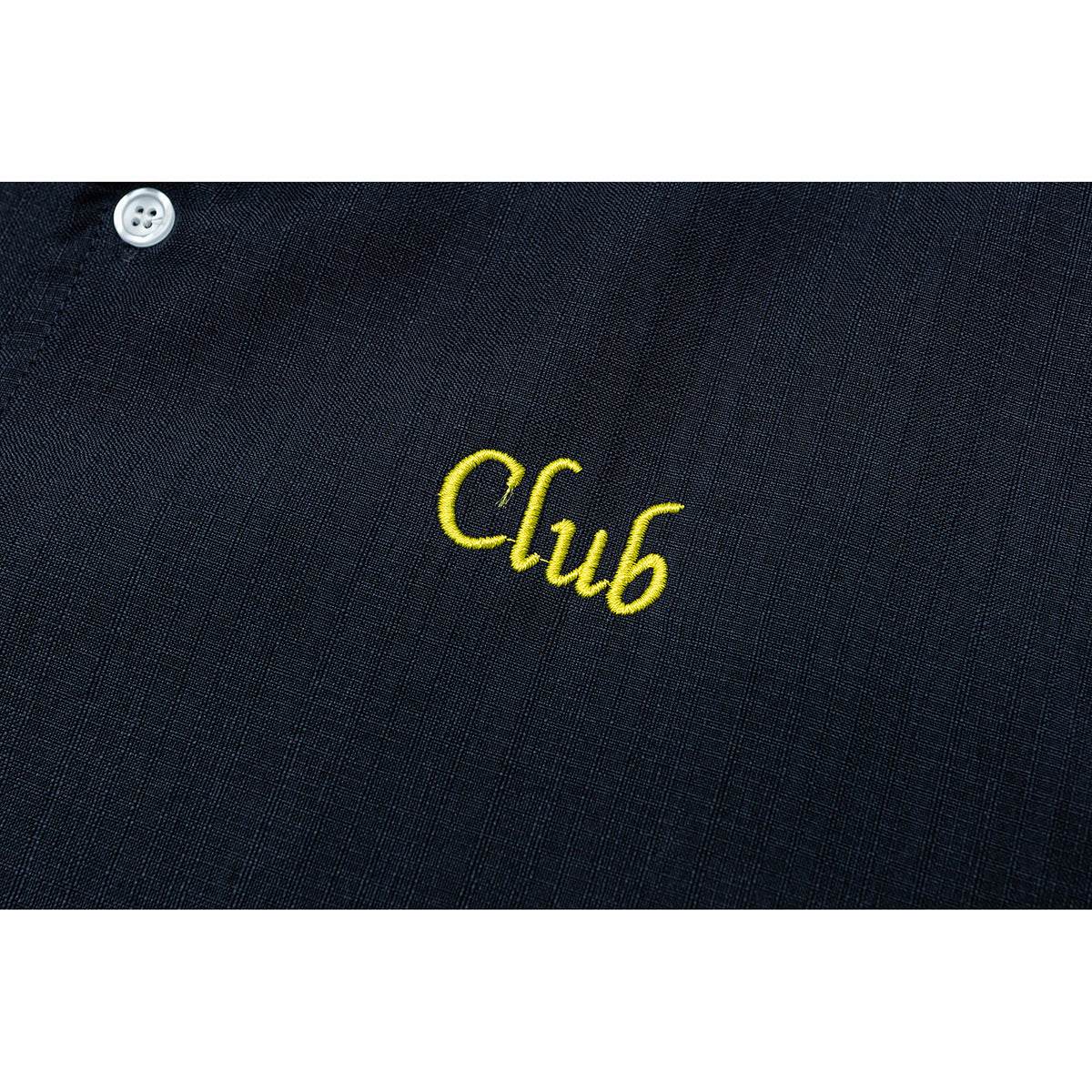 Close-up of yellow embroidered “Club” lettering on dark navy shirt fabric beside a white button.