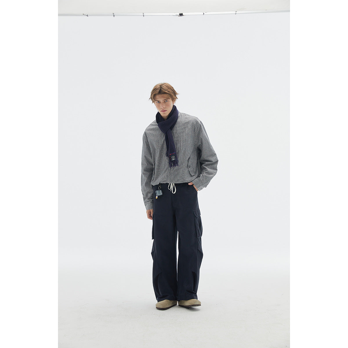 Model wearing a gray striped shirt, navy scarf, and loose dark cargo pants.