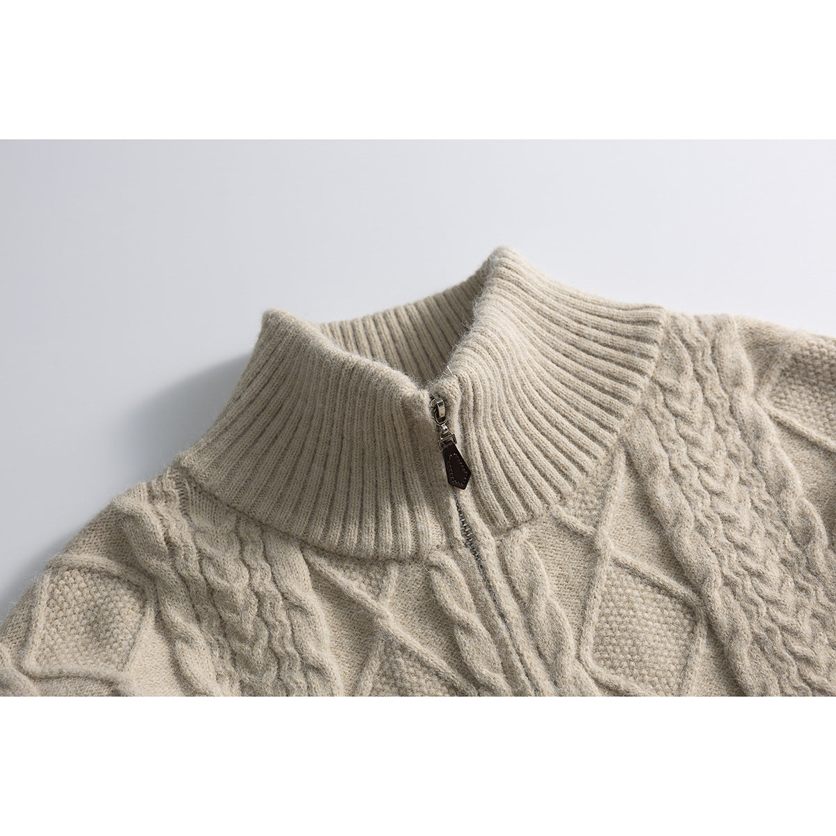 Close-up of a cream cable-knit sweater's ribbed high collar and front zipper.