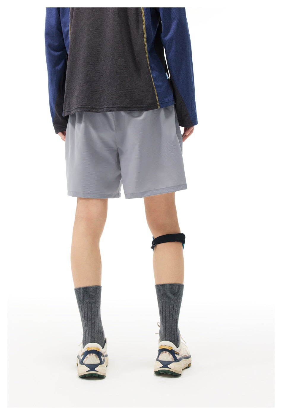 Rear view of a model wearing light gray athletic shorts with a dark blue and charcoal long-sleeve top.
