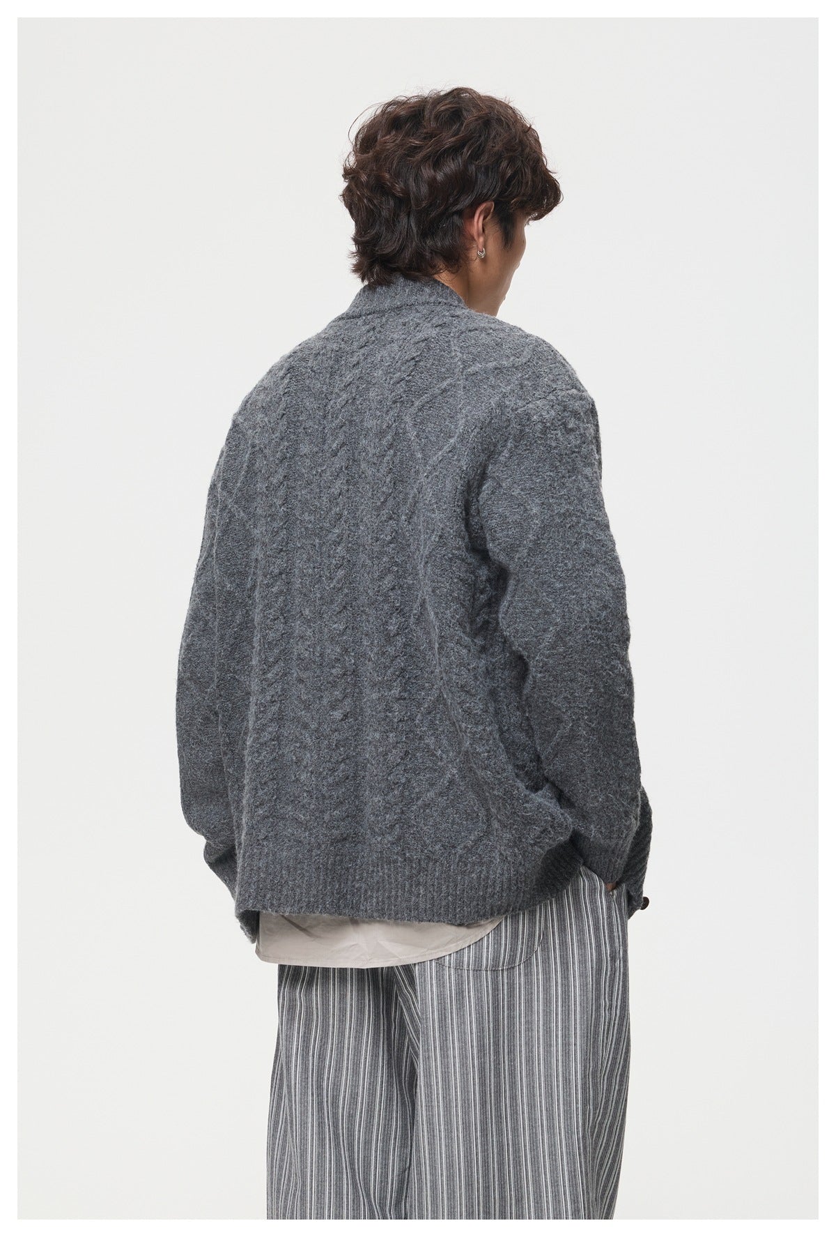 Back view of a model wearing a charcoal cable-knit cardigan with a ribbed hem.