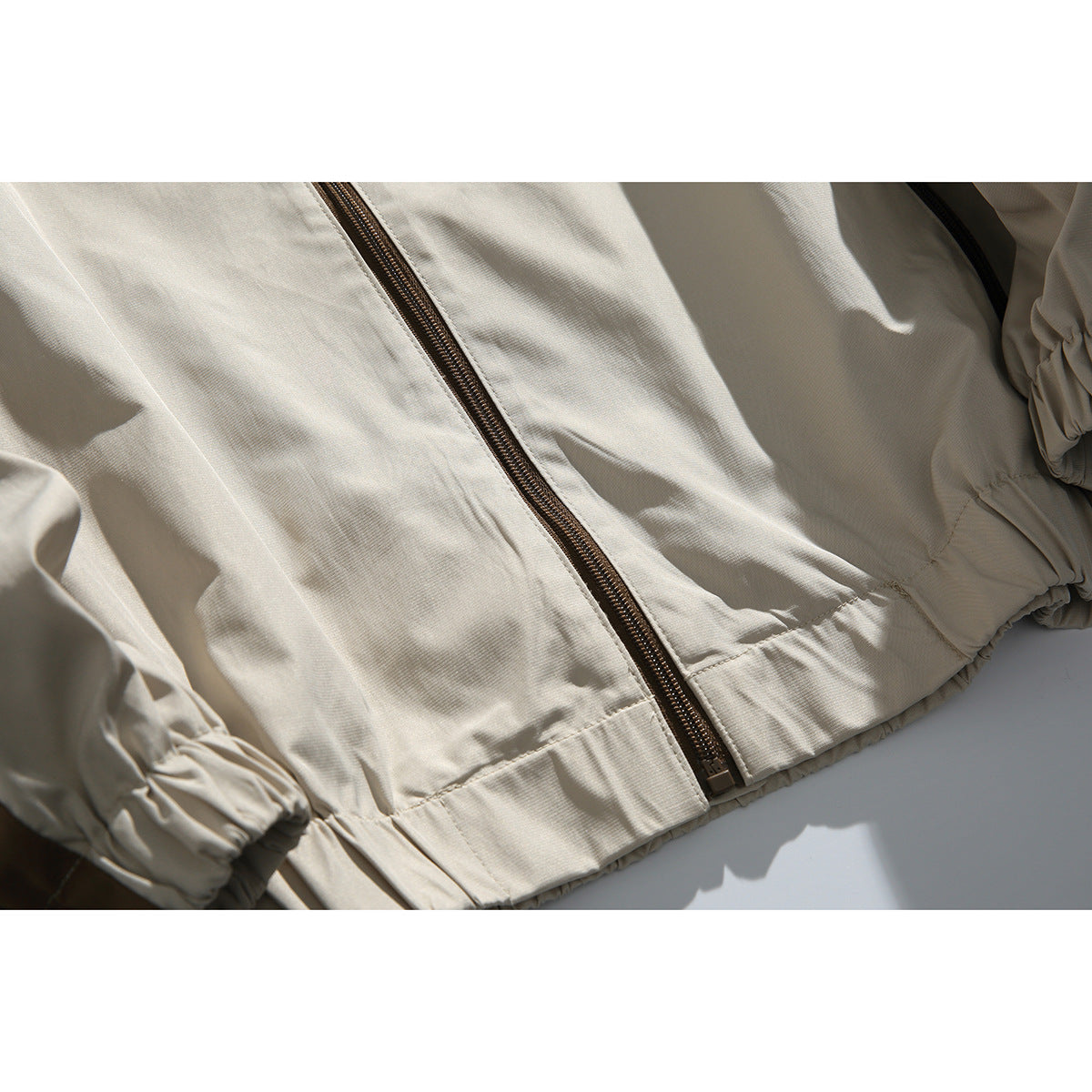 Close-up of a cream jacket showing its front zipper, gathered cuffs, and elastic hem.