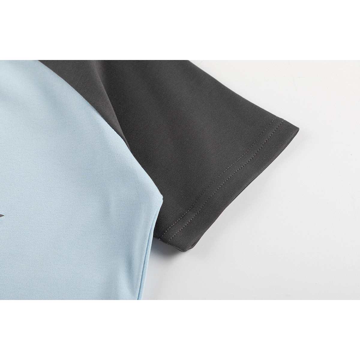 Close-up of the dark gray short sleeve and stitched hem on a light blue T-shirt.