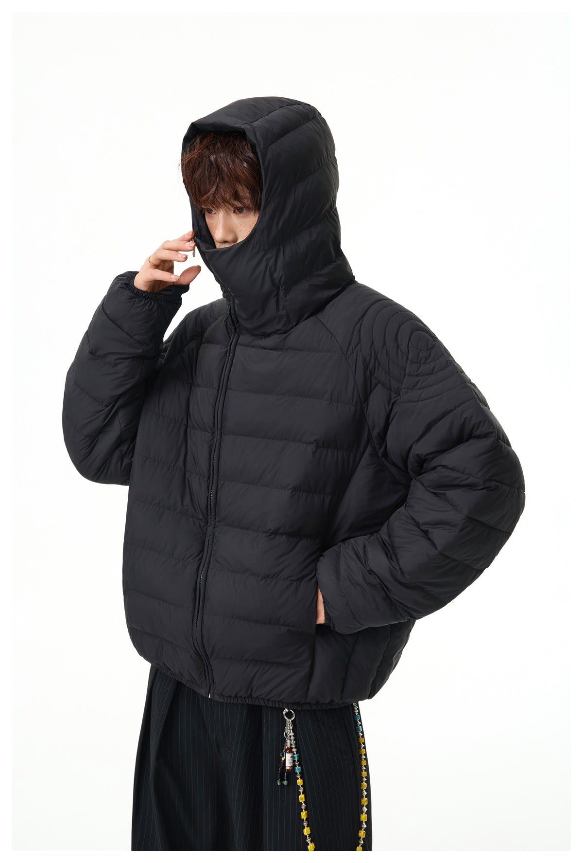 Model wearing the black quilted puffer jacket with its hood raised and face-covering collar fastened.