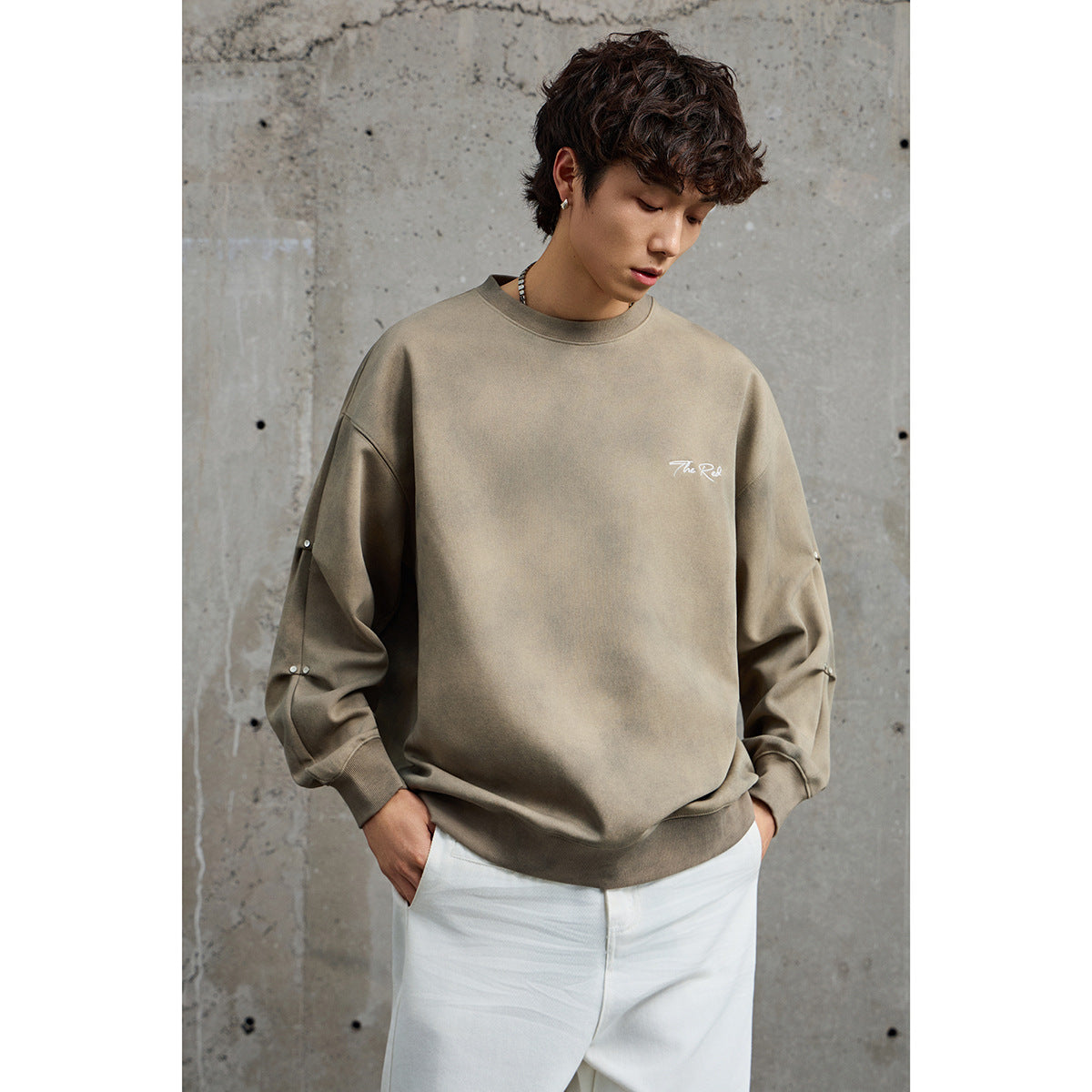 Close view of a model wearing a taupe sweatshirt with white chest script and metal sleeve studs.