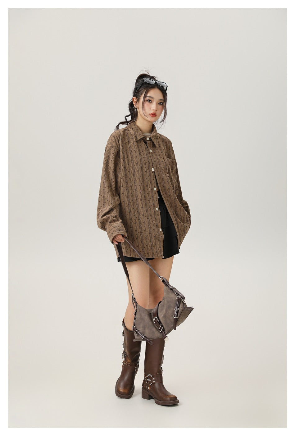 Model in an oversized brown patterned button-up shirt, black shorts, and tall brown boots, three-quarter front view.
