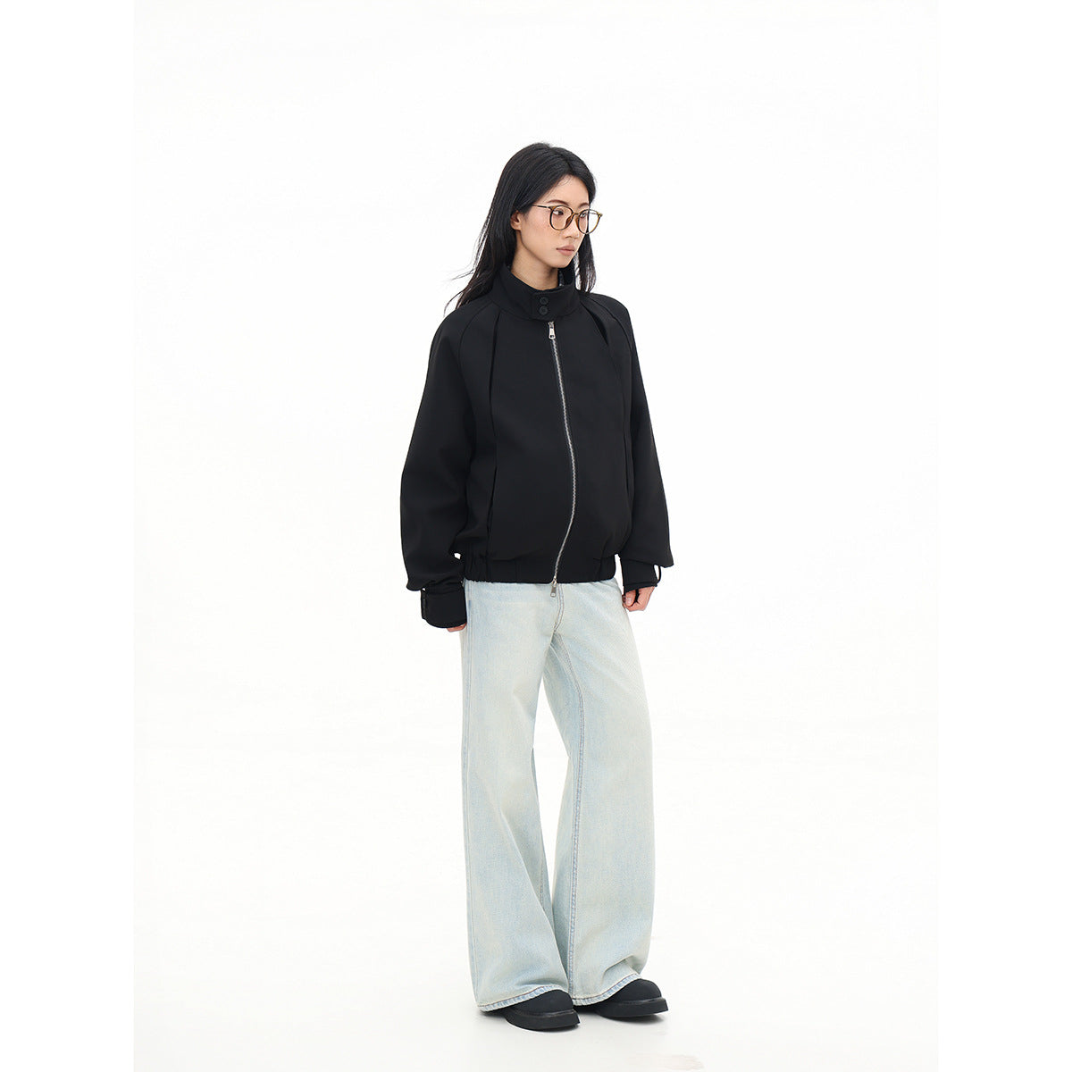 Model in a black zip-front jacket with a raised button collar and pale wide-leg jeans, shown at an angle.