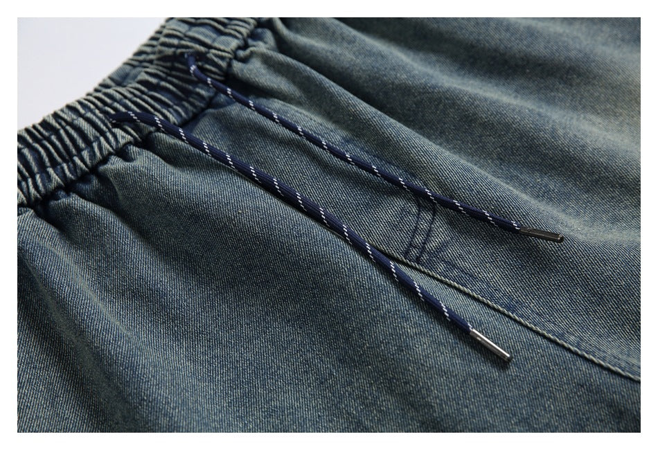 Close-up of blue denim pants showing the gathered elastic waist and navy drawstrings with metal tips.