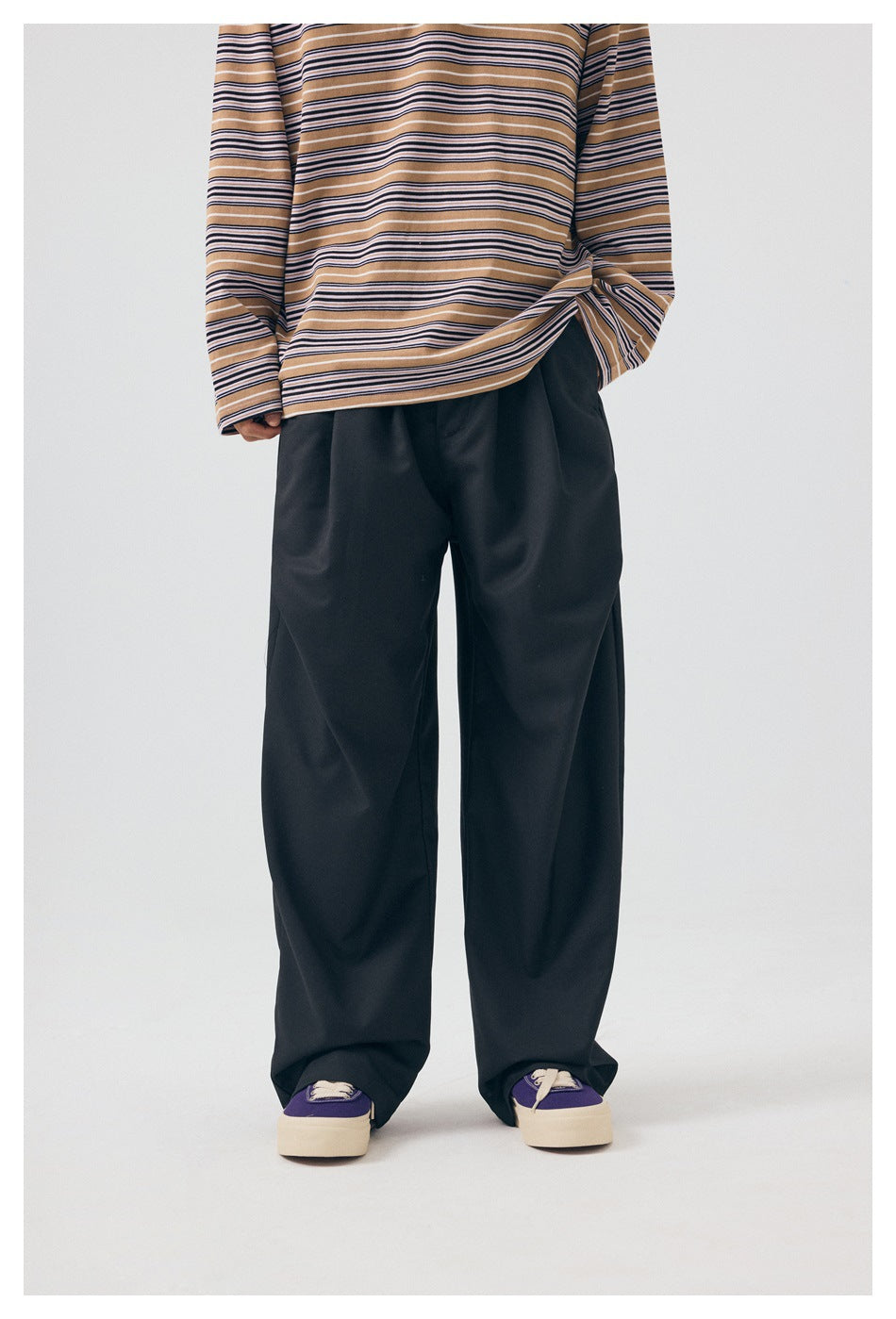 Cropped front view highlighting black wide-leg trousers and the hem of a tan striped long-sleeve shirt.