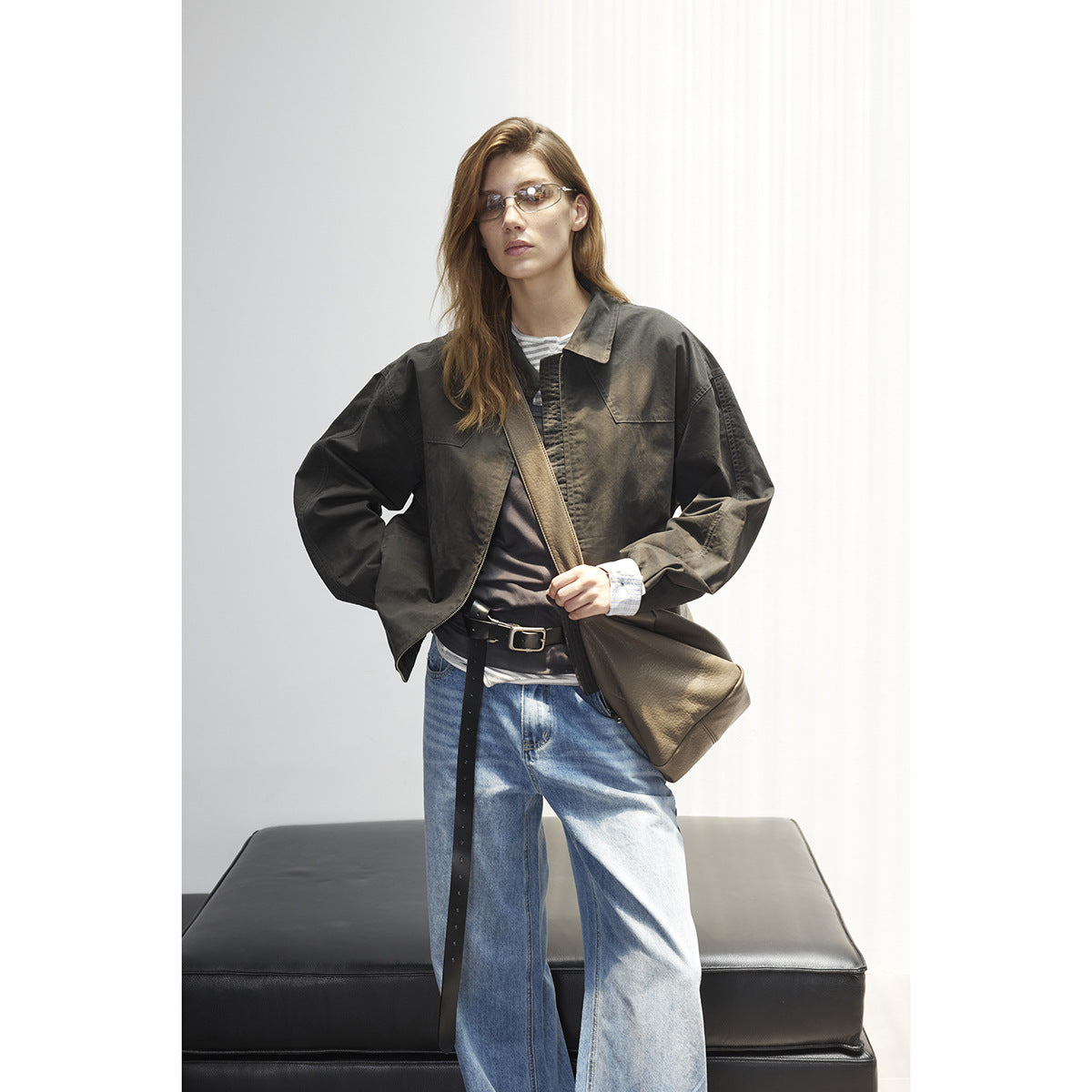 Model wearing an oversized charcoal collared jacket with checked cuffs, layered over a top and wide-leg blue jeans.