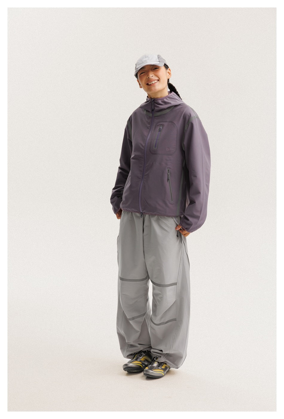 Model wearing a muted purple hooded zip jacket with gray pants featuring curved trim details.