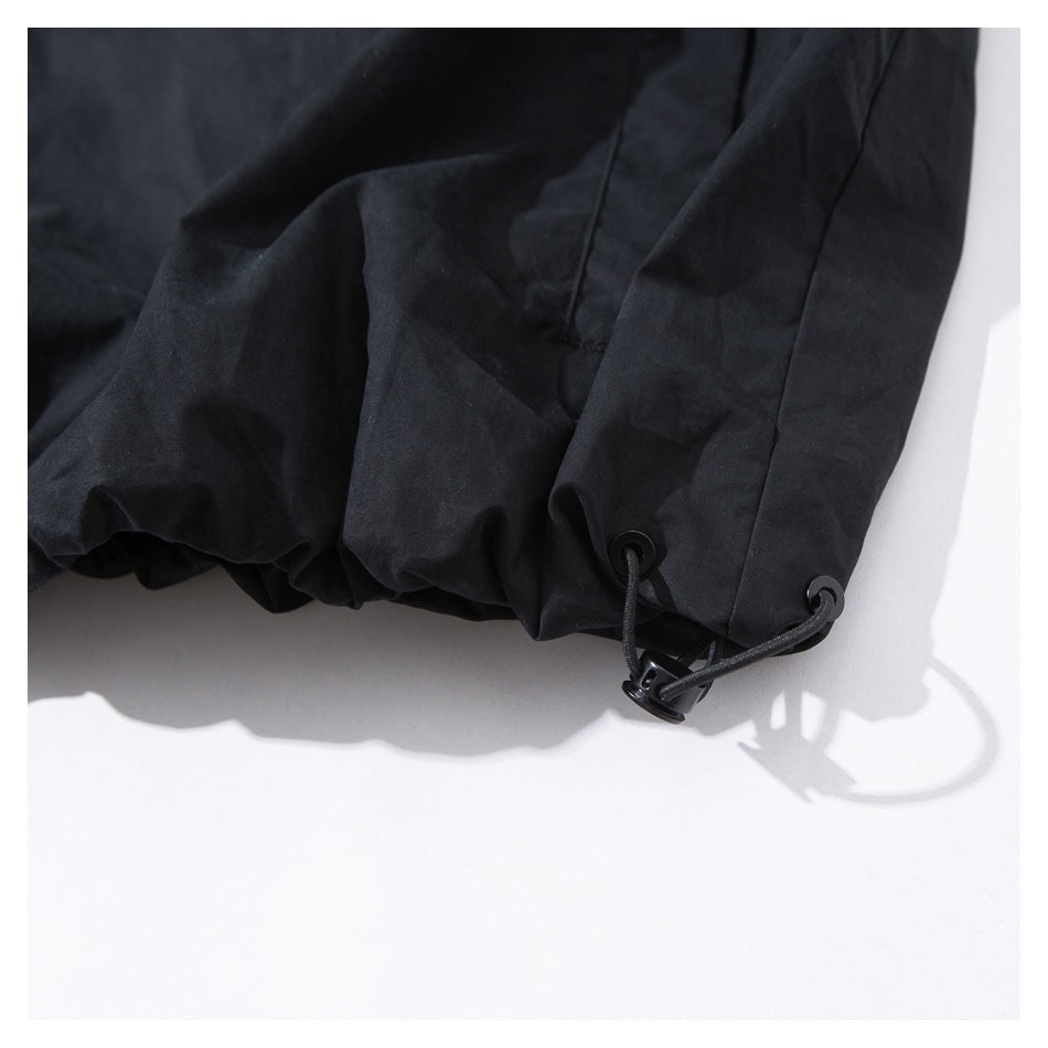 Close-up of a black garment hem with an adjustable drawcord, eyelets, and cord lock.