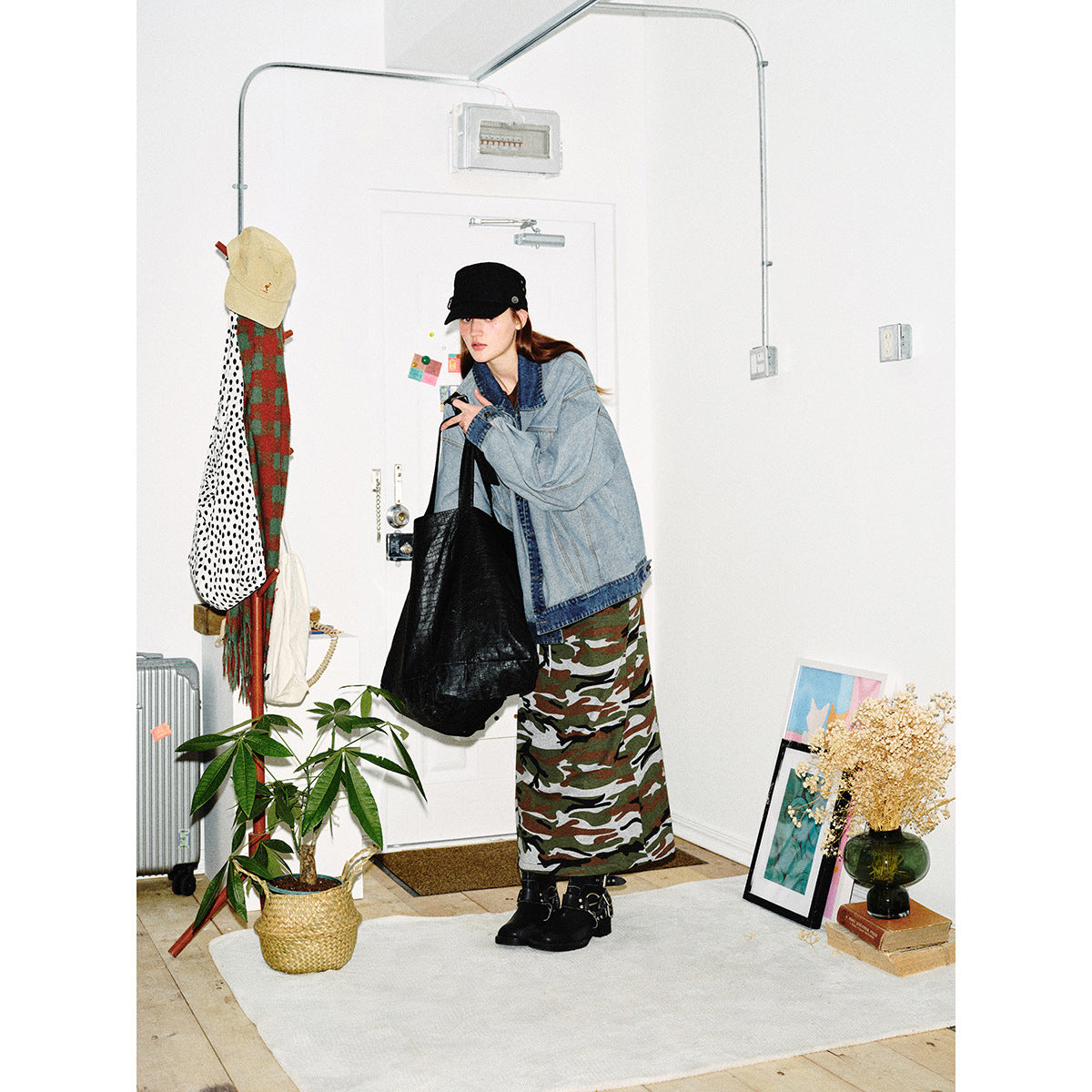 Model in an oversized light-wash denim jacket and long camouflage skirt, carrying a black tote.