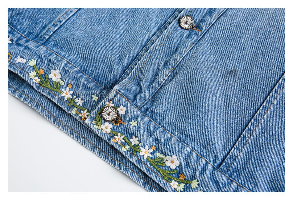Close-up of a blue denim jacket hem with white and yellow floral embroidery and decorative buttons.
