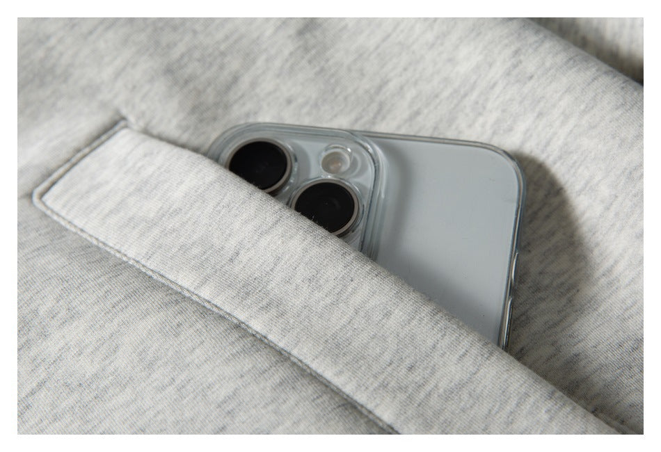 A phone tucked into the pocket of a light gray marled sweatshirt, showing the pocket opening.