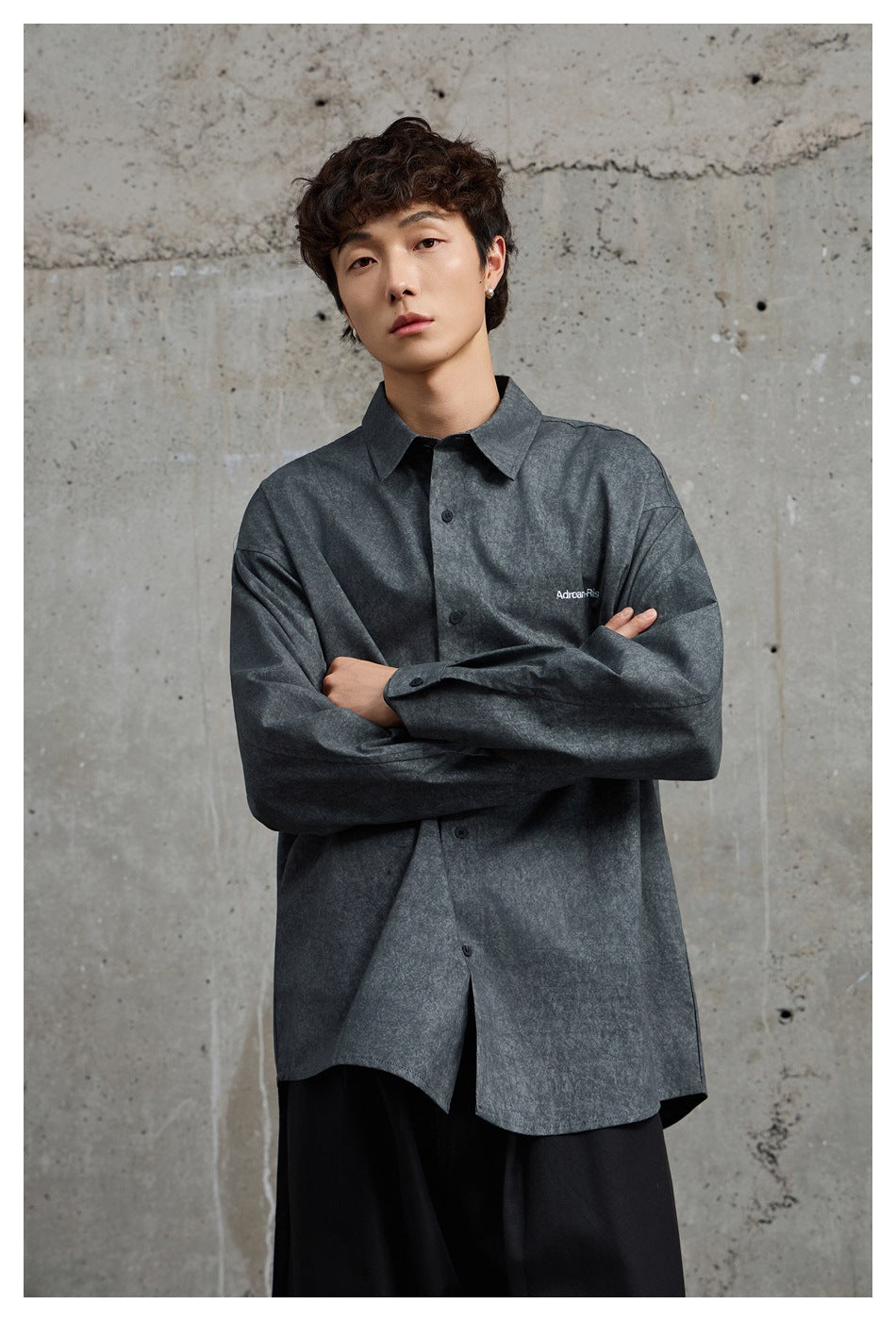 Close-up of a model in an oversized black gray washed-look shirt with a pointed collar, arms crossed