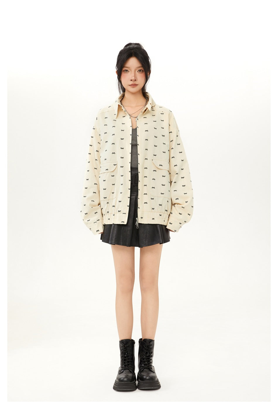 Model wearing an open bow-print apricot jacket with a gray top, black pleated skirt and black boots, front view