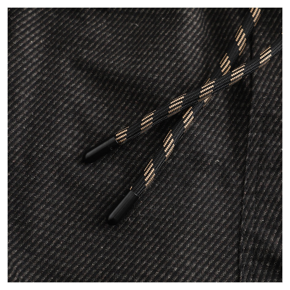 Close-up of black drawstrings with tan accents and plastic tips on dark striped pants.