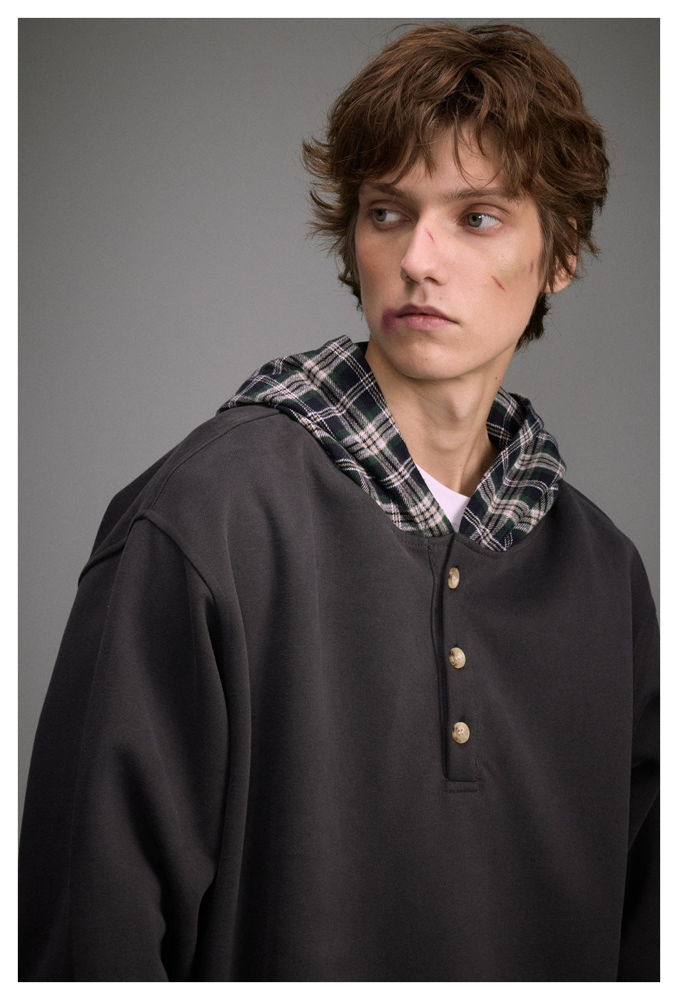 Close view of a man wearing a charcoal pullover with a plaid-lined hood and three-button placket.