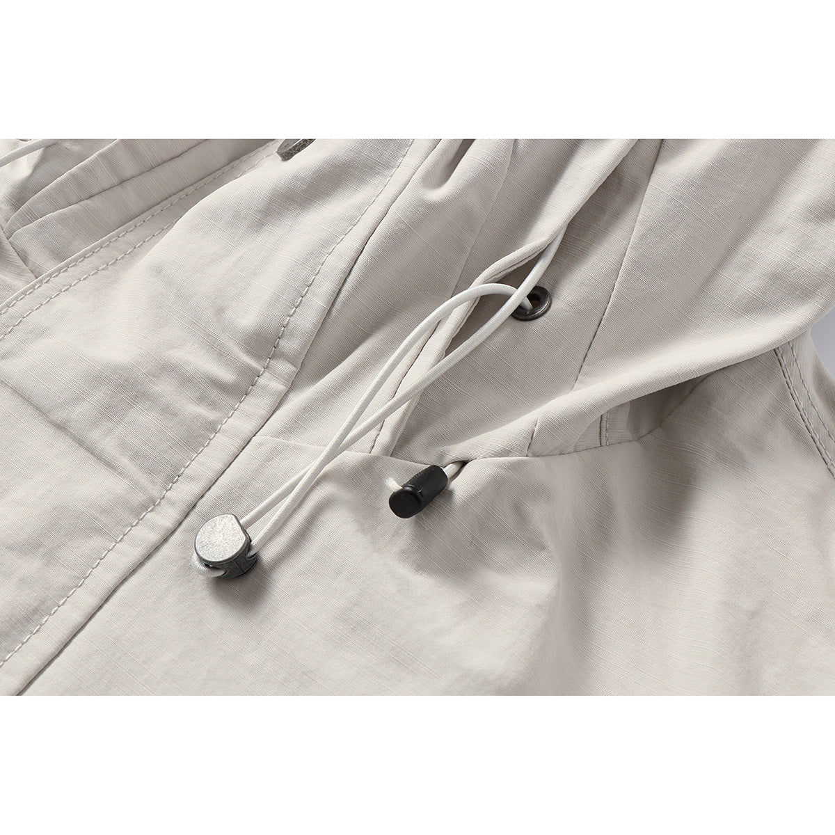 Close-up of an off-white hooded jacket's adjustable drawcords, eyelet, and toggles.