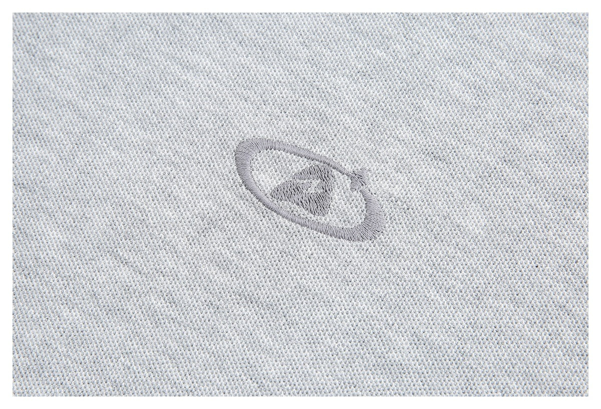Close-up of a small gray embroidered oval emblem on light gray knit fabric.